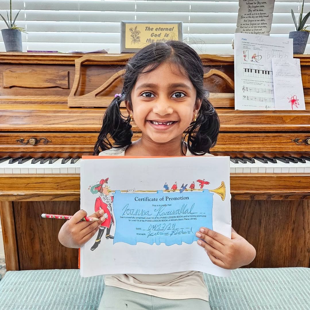 A student holding her certificate of promotion at the piano